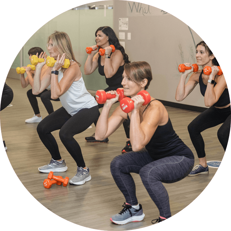 Group strength session at well studio with students squatting while holding dumbbells in each hand.