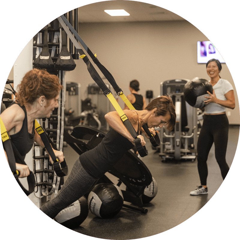 Personal Trainer watches as students lean forward to pull weights with arm straps.