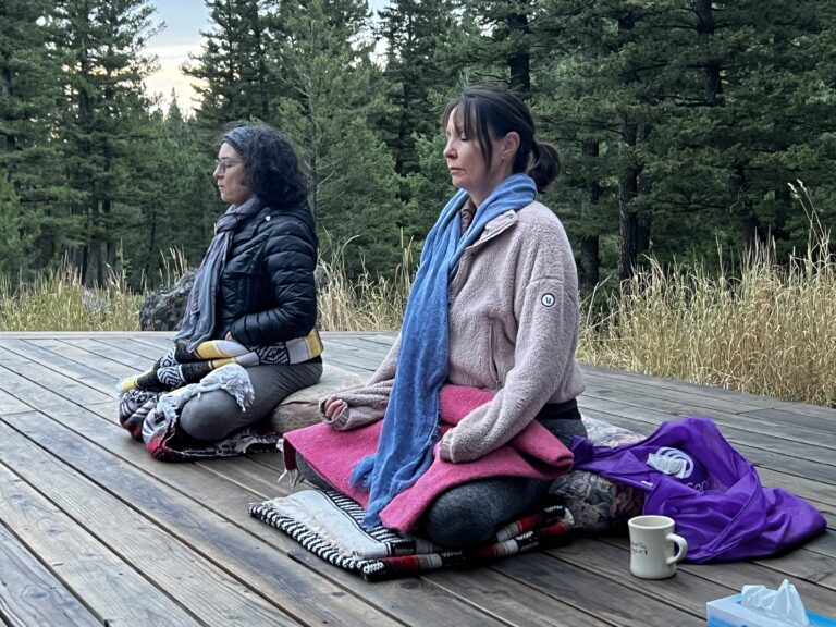 Stacy and Teresa seated cross legged, meditating on the yoga deck at Feathered Pipe Ranch