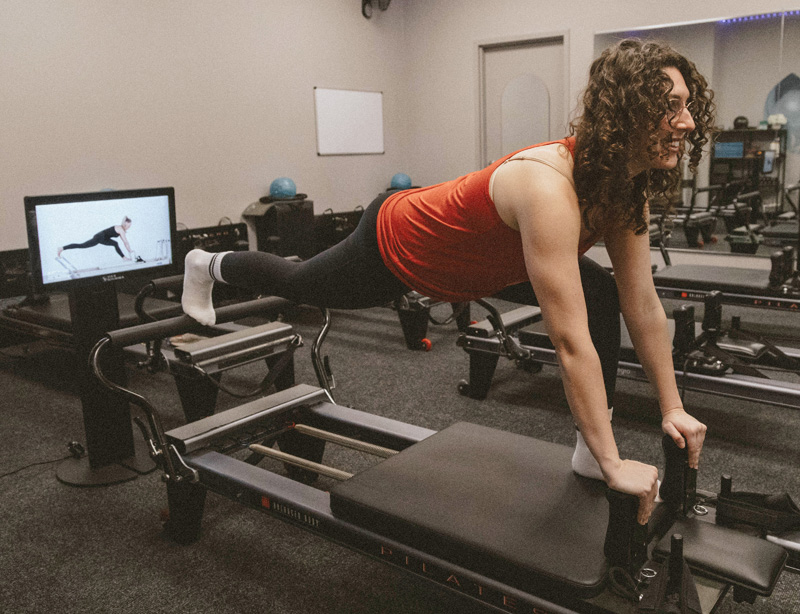 A female Well Studio member stretching on a Pilates Reformer while using the KioskPro.