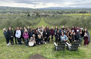 A group of women on a yoga retreat standing in an olive tree orchard overlooking a green valley